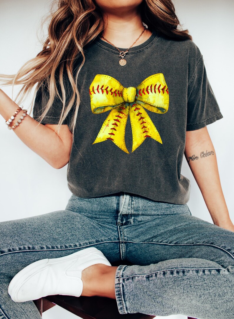 K&ouml;nnte beinhalten: Ein anthrazitfarbenes T-Shirt mit einem gelben Softball-Schleifen-Motiv. Die Schleife ist mit rotem Garn gestickt und hat einen Aquarell-Effekt.
