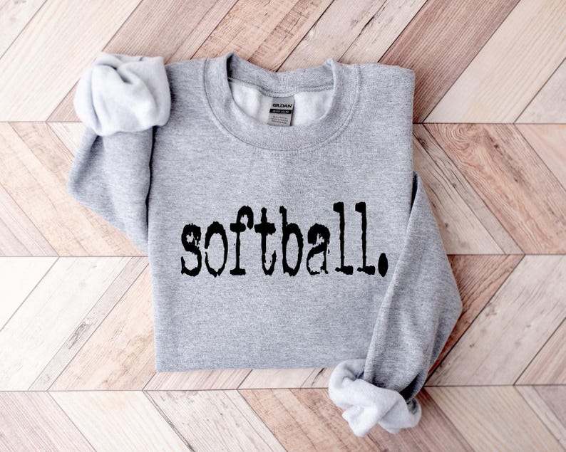 K&ouml;nnte beinhalten: Ein grauer Pullover mit dem Wort "Softball" in Schwarz auf der Vorderseite.
