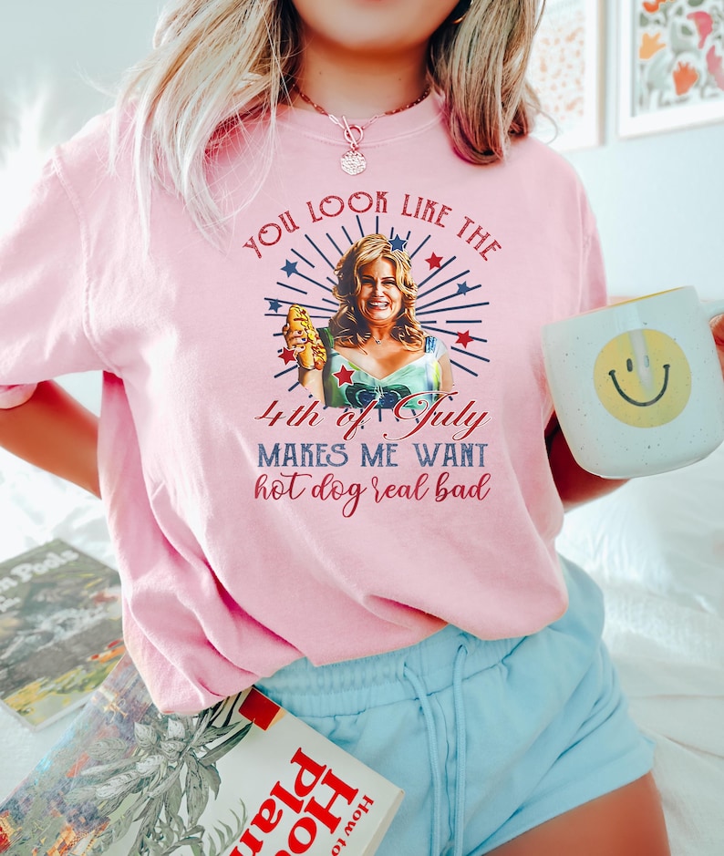 May include: A pink t-shirt with a graphic of a woman holding a hot dog and the text "You look like the 4th of July makes me want hot dog real bad".