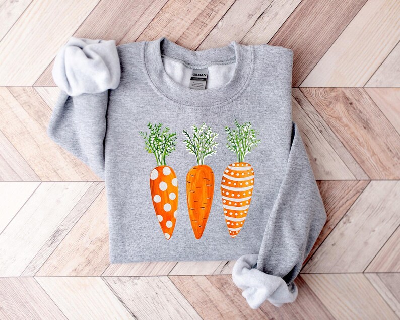 Puede incluir: Una sudadera gris con un dise&ntilde;o de tres zanahorias naranjas con lunares blancos y rayas. Las zanahorias tienen hojas verdes.