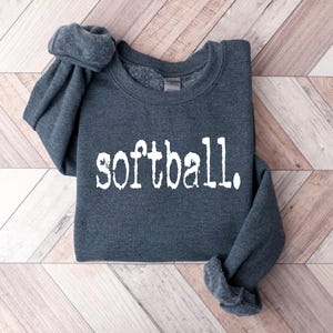 K&ouml;nnte beinhalten: Ein dunkelgrauer Pullover mit dem Wort "Softball" in wei&szlig; auf der Vorderseite.