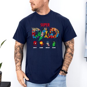 May include: A navy blue t-shirt featuring the text "SUPER DAD" in red, with a collage of superhero characters forming the letters. Below are four cartoon superhero figures, each with a name: Amity, Alger, Devlin, and Alvar.