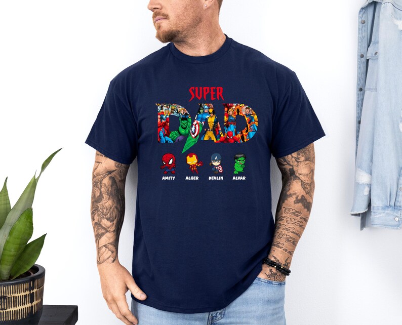 May include: A navy blue t-shirt featuring the text "SUPER DAD" in red, with a collage of superhero characters forming the letters. Below are four cartoon superhero figures, each with a name: Amity, Alger, Devlin, and Alvar.