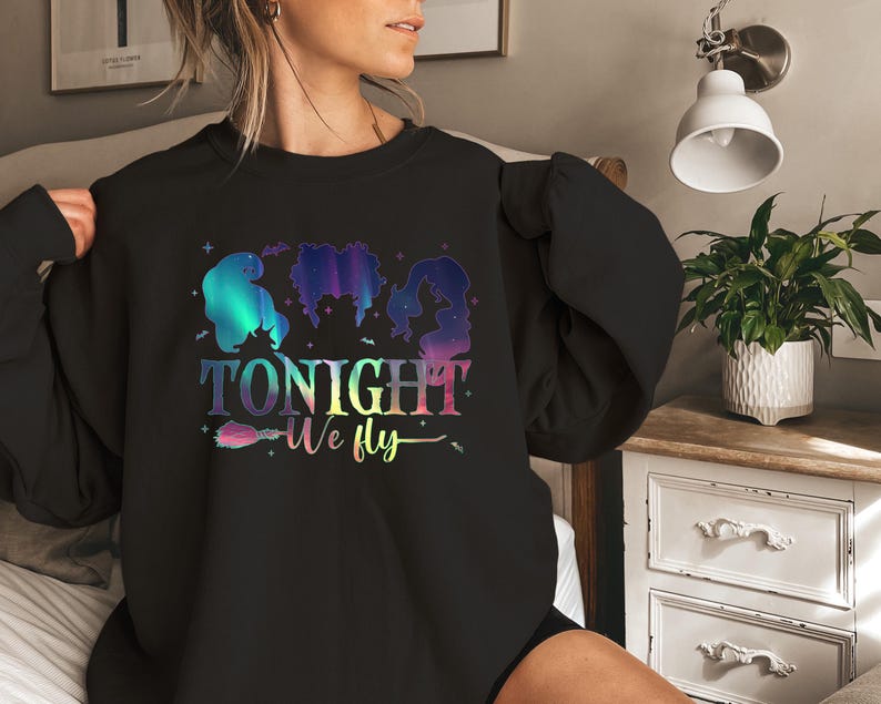 May include: Black sweatshirt with a colorful graphic featuring three witch silhouettes and the text "TONIGHT We fly". The design includes a broom and stars, with a gradient color scheme.