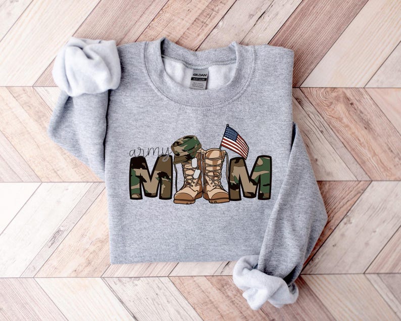 May include: Gray sweatshirt with a camouflage print that says "army mom" with a pair of boots and a military hat. There is an American flag above the boots.