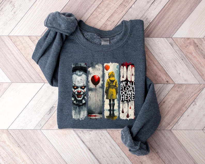 May include: Dark gray sweatshirt featuring a graphic design with a scary clown, a person in a yellow raincoat, and the text "WE ALL FLOAT DOWN HERE". The design includes red balloons and dripping blood.