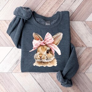May include: A dark blue sweatshirt with a graphic of a brown bunny wearing a pink and white bow. The bunny is looking directly at the viewer.