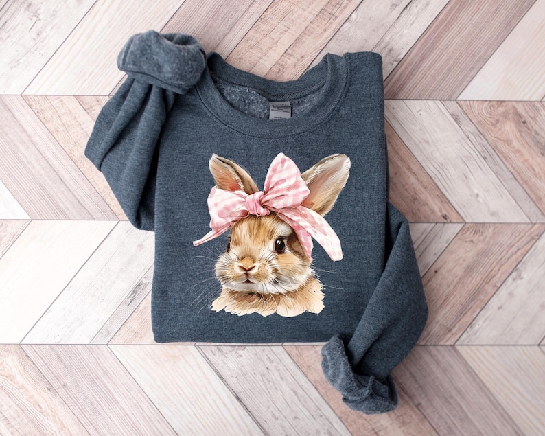 May include: A dark blue sweatshirt with a graphic of a brown bunny wearing a pink and white bow. The bunny is looking directly at the viewer.