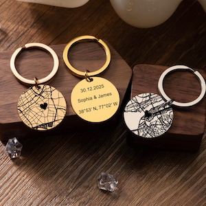 May include: Three personalised keyrings with round pendants. One gold keyring features a map design with a heart, another gold keyring has the text "30.12.2025 Sophia & James 38°53' N, 77°02' W". The third keyring has a map design.