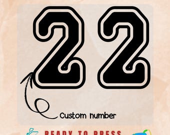 May include: A DTF transfer featuring the number 22 in a bold black font with a white outline. The text DTF TRANSFER appears at the top, while the words READY TO PRESS are at the bottom. A hand-drawn arrow points to the number with the text Custom number.