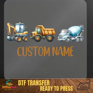 Puede incluir: Transferencia DTF con tres veh&iacute;culos de construcci&oacute;n: una excavadora, un cami&oacute;n volquete y una hormigonera. El texto "CUSTOM NAME" es naranja. El texto inferior dice "DTF TRANSFER READY TO PRESS".