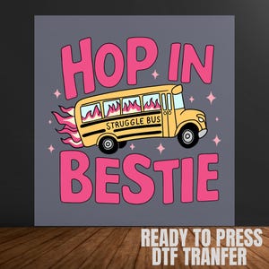 May include: A graphic design featuring a yellow school bus with the words "STRUGGLE BUS" on the side, flames, and the text "HOP IN BESTIE" in pink. The background is gray with pink star accents.