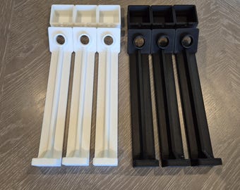 Puede incluir: Dos juegos de componentes de plástico impresos en 3D. Un juego es blanco y el otro negro. Cada juego incluye tres piezas rectangulares con una parte superior cuadrada, un agujero circular y una extensión rectangular larga y plana.