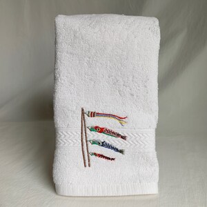 May include: White hand towel with embroidered colorful Japanese carp streamers, also known as koinobori, on a white background.