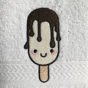 May include: Embroidered white popsicle with a brown chocolate drizzle and a smiling face. The popsicle has a brown stick.