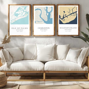 Puede incluir: Tres impresiones enmarcadas de mapas de las zonas costeras de Carolina del Sur: Isle of Palms, Charleston y Sullivan's Island. Cada mapa presenta una paleta de colores única y está enmarcado en un marco de madera natural. Las impresiones se muestran sobre un sofá color crema.