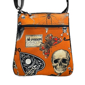 May include: Orange crossbody bag with a black zipper and strap. The bag features a skull and crossbones, a butterfly, a spider web, and a Ouija board with the text "Hello Goodbye Yes No".