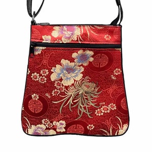 May include: A red crossbody bag with a black strap and a floral pattern. The bag has two zippered compartments and a black trim.