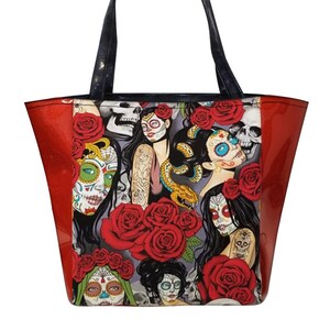 May include: Red and black tote bag with a colorful print of sugar skulls, roses, and women. The bag has black handles.