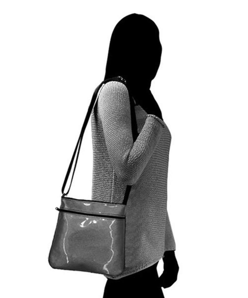 K&ouml;nnte beinhalten: Eine schwarze Umh&auml;ngetasche mit einem silbernen Rei&szlig;verschluss und einem gl&auml;nzenden, strukturierten Finish. Die Tasche wird &uuml;ber der Schulter einer Person getragen.