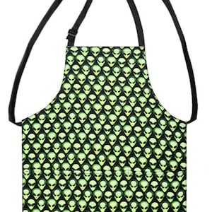 May include: Black apron with a green alien face pattern. The apron has two adjustable straps and a large pocket.