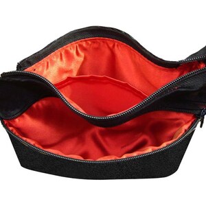 K&ouml;nnte beinhalten: Schwarze Rei&szlig;verschlusstasche mit rotem Satin-Futter. Die Tasche hat zwei F&auml;cher.