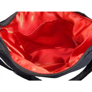 K&ouml;nnte beinhalten: Eine schwarze Tasche mit Rei&szlig;verschluss und roter Satinfutter. Die Tasche hat eine kleine Innentasche.