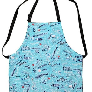 May include: A light blue apron with black straps, featuring a pattern of medical symbols and words like "Thank You," "Superheroes," and "Brave." The apron has two pockets and is designed for healthcare professionals.
