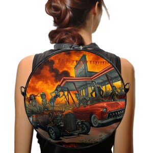 Könnte beinhalten: Runder schwarzer Rucksack mit einer farbenfrohen Illustration einer Zombie-Diner-Szene. Das Bild zeigt Oldtimer, Zombies und den Text "Zombie Drive-In" vor einem feurigen orangefarbenen Himmel.