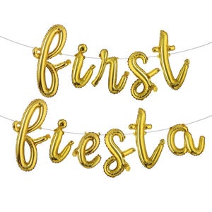 May include: Gold foil balloons spelling out "First Fiesta" strung on a thin white string. The balloons are in a cursive font, perfect for a festive celebration. The balloons are inflated and ready to hang.