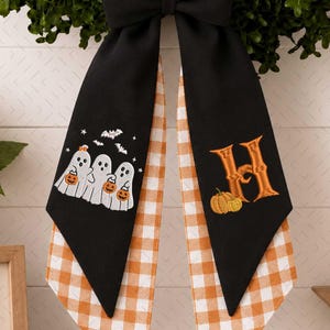 Peut inclure: Un nœud en tissu noir avec deux longs pans présentant un motif vichy blanc et orange sur l'envers. Un pan affiche trois fantômes blancs tenant des citrouilles orange, tandis que l'autre pan présente une grande lettre H orange avec une citrouille.