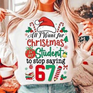 May include: White sweatshirt featuring a Christmas design. The graphic includes a Santa hat, candy canes, and the text "All I Want for Christmas is my Student to stop saying 67". A festive and humorous garment.