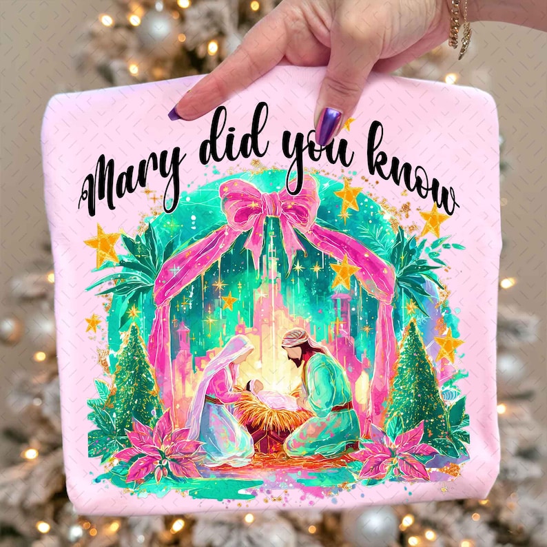 May include: A pink, square-shaped item with the text "Mary did you know" in black script. The image features a Nativity scene with Mary, Joseph, and baby Jesus, surrounded by a decorative arch and stars. The design includes pink, green, and gold accents.