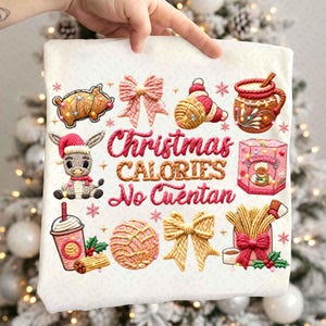 May include: White Christmas-themed fabric with embroidered images of festive treats and a donkey wearing a Santa hat. The text "Christmas Calories No Cuentan" is also embroidered in red and gold. The design includes a pig, bows, and a box of cookies.
