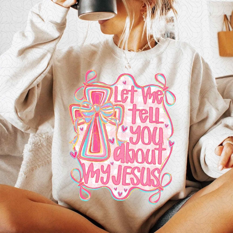 K&ouml;nnte beinhalten: Cremefarbenes Sweatshirt mit rosa und blauer Grafik. Die Grafik zeigt ein Kreuz mit einer Schleife und den Text "Let Me Tell You About My Jesus" in rosa Schrift. Das Design ist rosa umrandet.