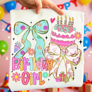 May include: White t-shirt with a colorful birthday design. The design includes a large bow, a birthday cake with candles, and the words "Birthday Girl" in a playful font. The design also features gift boxes and floral accents.