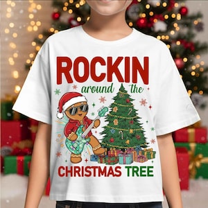 May include: White t-shirt with a Christmas-themed graphic. The design features a gingerbread man wearing sunglasses and a Santa hat, playing a guitar in front of a decorated Christmas tree. The text "ROCKIN' around the CHRISTMAS TREE" is printed above and below the image.