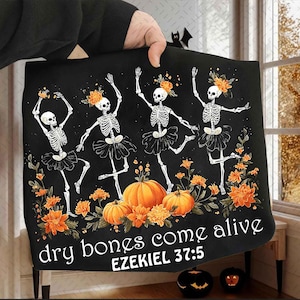 May include: Black Halloween-themed blanket featuring dancing skeletons in tutus with orange flower crowns. Pumpkins and flowers are at the bottom, with the text "dry bones come alive" and "EZEKIEL 37:5".