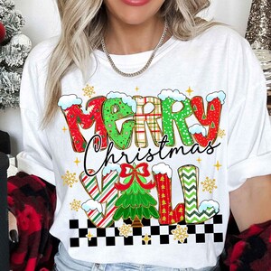 May include: White t-shirt with a festive "MERRY Christmas Y'ALL" design. The text features a mix of red, green, and plaid patterns, with snowflakes and a Christmas tree graphic. The shirt has a black and white checkered border.