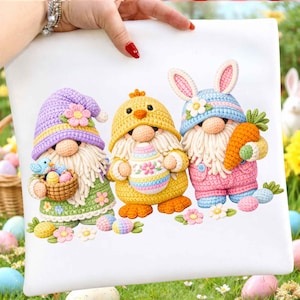 May include: A white pillow featuring three Easter-themed gnomes. One gnome wears a purple hat and holds a basket with a blue bird and eggs. The second gnome is a chick holding an Easter egg. The third gnome wears a bunny hat and holds a carrot.