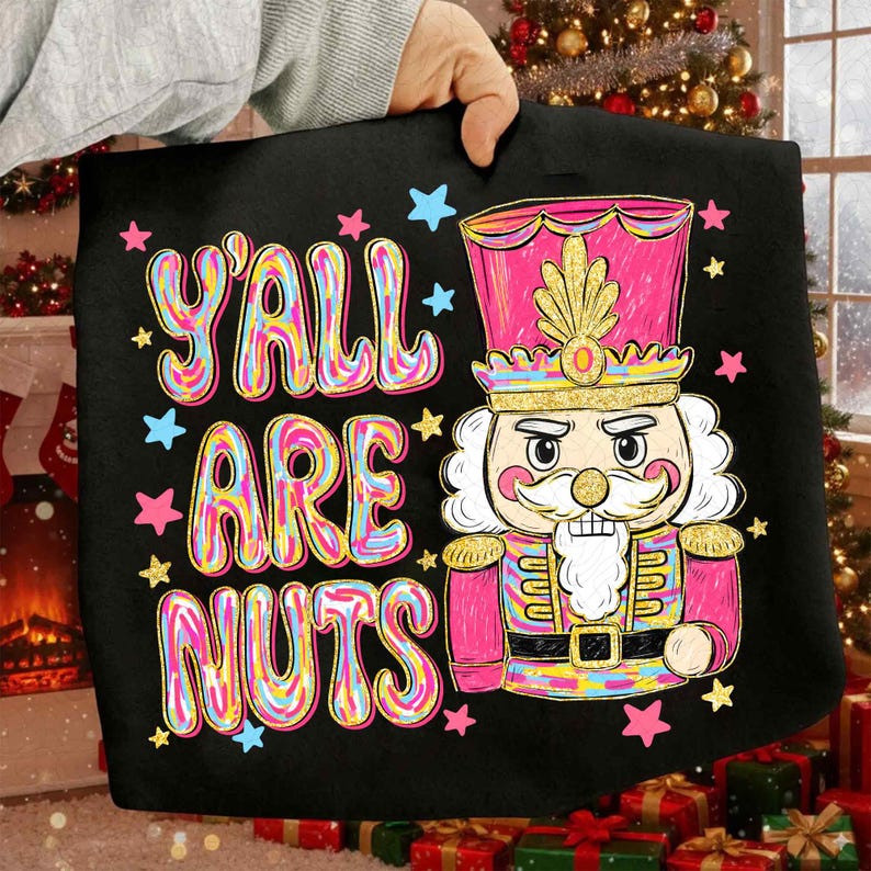 May include: Black tote bag with the text "Y'ALL ARE NUTS" in colorful bubble letters, surrounded by stars. A pink and gold nutcracker soldier is featured on the right side of the bag, with a gold crown and a white beard.