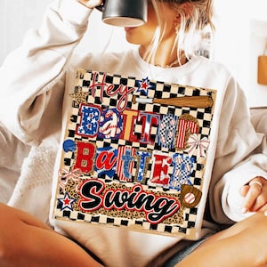 Può includere: Felpa bianca con grafica a tema baseball. La grafica presenta le parole "Hey Batter Batter Swing" in rosso, bianco e blu, con mazze da baseball, stelle e palline da baseball. Il design è ambientato su uno sfondo a scacchi e leopardato.
