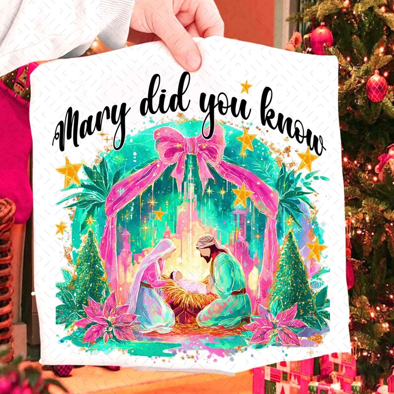 May include: A white decorative pillow featuring a Nativity scene with the text "Mary did you know". The design includes Mary, Joseph, and baby Jesus, surrounded by a pink bow, stars, and Christmas trees. The pillow is held by a person.