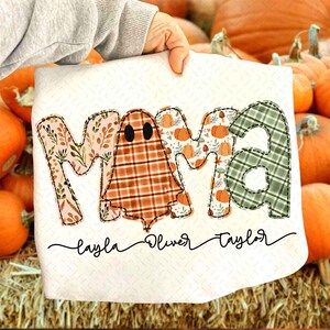 May include: A white decorative towel with the word "MAMA" in a patchwork design. The "M" is floral, the "A" is plaid, and the middle "M" is a ghost. Below are the names "Layla", "Oliver", and "Taylor".