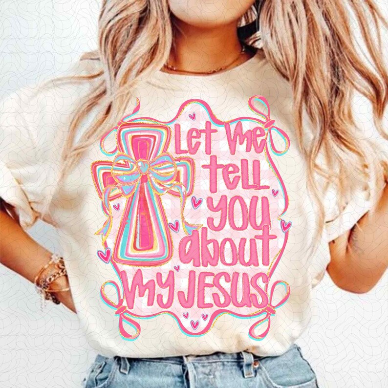 K&ouml;nnte beinhalten: Cremefarbenes T-Shirt mit einem rosa Kreuz mit Schleife und dem Text "Let Me Tell You About My Jesus" in Rosa. Das Design enth&auml;lt blaue und gelbe Akzente und kleine Herzdetails.
