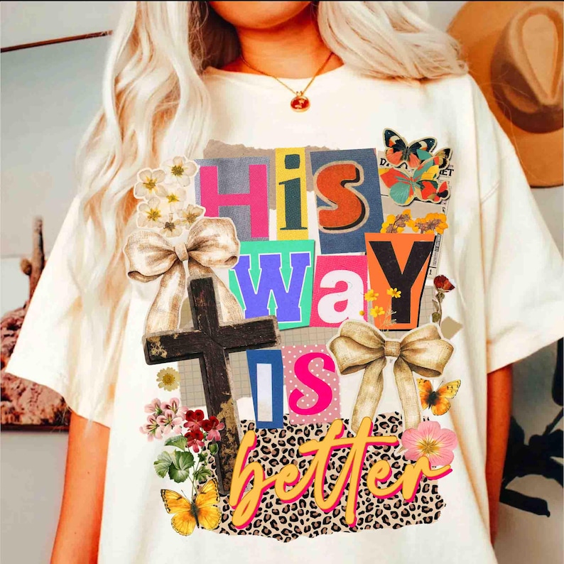May include: Cream-colored t-shirt with the text "His Way Is Better" in a collage style. The design includes a cross, butterflies, flowers, and bows. The letters are in various colors and fonts.