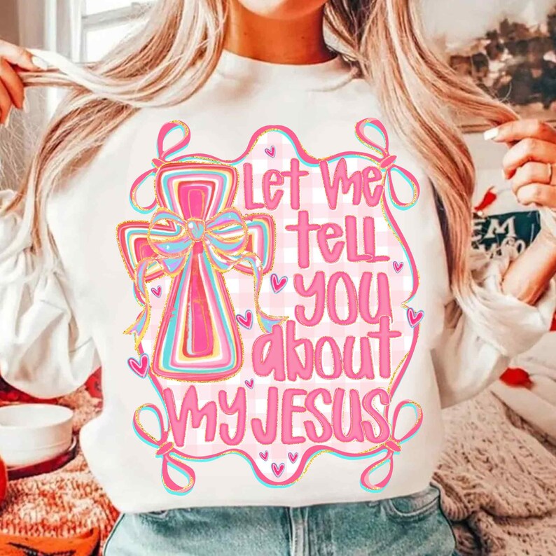 K&ouml;nnte beinhalten: Wei&szlig;es Sweatshirt mit einem rosa und blauen Kreuzdesign und dem Text "Let Me Tell You About My Jesus". Die Grafik hat einen karierten Hintergrund und Herzakzente. Das Design ist in einem verspielten, farbenfrohen Stil gehalten.