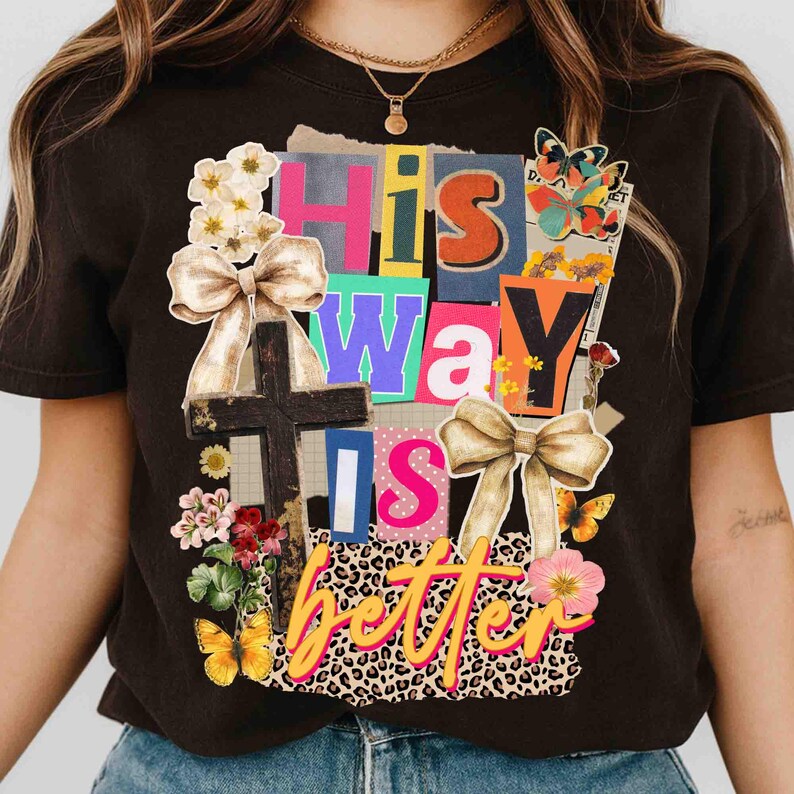 May include: Dark brown t-shirt with a colorful collage design. The design includes the words "His Way Is Better" in various fonts and colors, a wooden cross, bows, flowers, and butterflies.