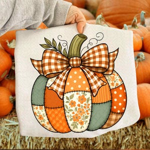 May include: A decorative cushion with a patchwork pumpkin design. The pumpkin has segments of orange polka dots, floral patterns, and green fabric. A large orange and white checked bow sits atop the pumpkin, with a green stem and leaves.