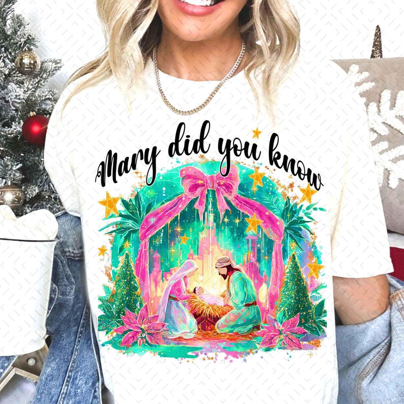 May include: White t-shirt with the text "Mary did you know" in black script. The shirt features a colorful graphic of the Nativity scene with pink ribbons, stars, and Christmas trees. The design is festive and holiday-themed.